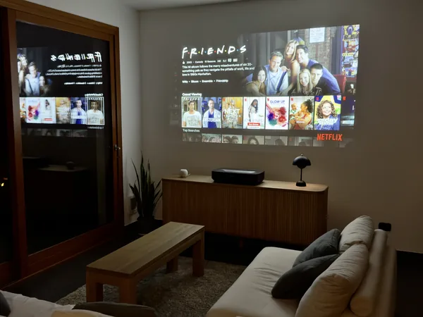 The 100-inch laser projector filling the living room wall with a streaming menu