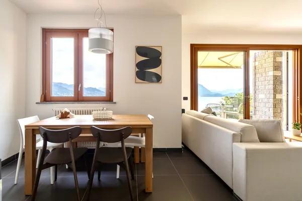 Dining table and chairs beside the window, with the terrace door open to the lake