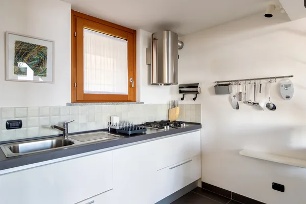 Fully equipped white kitchen with gas hob, sink and a window over the counter