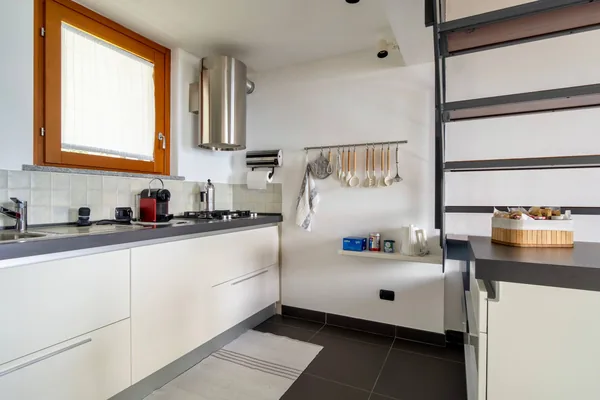 Kitchen units and extractor beside the open staircase, with a dark tiled floor