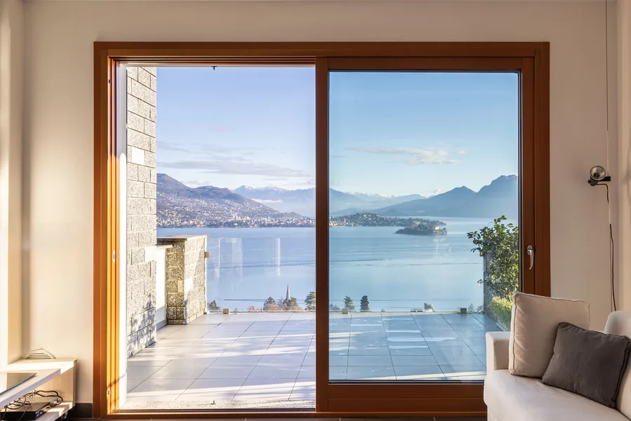 Full-height sliding doors framing a panoramic view of Lake Maggiore, with a window seat beside them