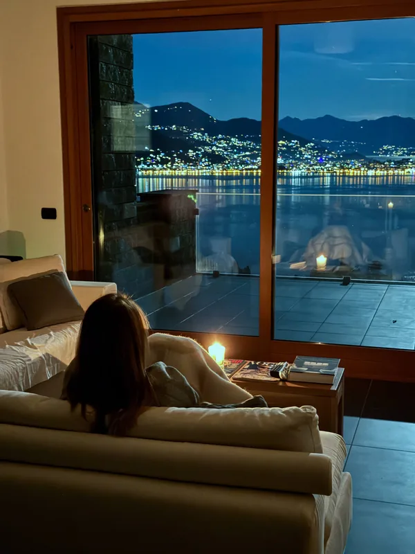 Sitting on the sofa at night, looking through the full-height window at the lights across the lake