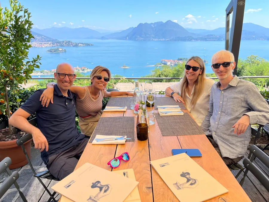 Alex, Vero, Alice and Nicolò around a table on the terrace, with Lake Maggiore behind them