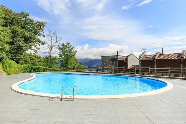 Oval swimming pool with a wide paved sun deck and mountains behind